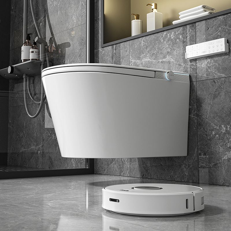 A modern bathroom features the Refurne Modern Japanese Wall-Mounted Smart Toilet with heated seat, remote control, and advanced hygiene features on gray tiles, plus a robotic vacuum; shelves and a shower area adorn the wall.