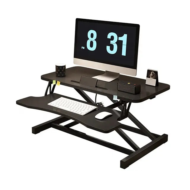 The Refurne Height Adjustable Standing Desk Riser Table in black holds a monitor showing the time, a keyboard on its lower tray, plus desk items like a mug, photo frame, pen holder, and small speaker for an ergonomic workstation.