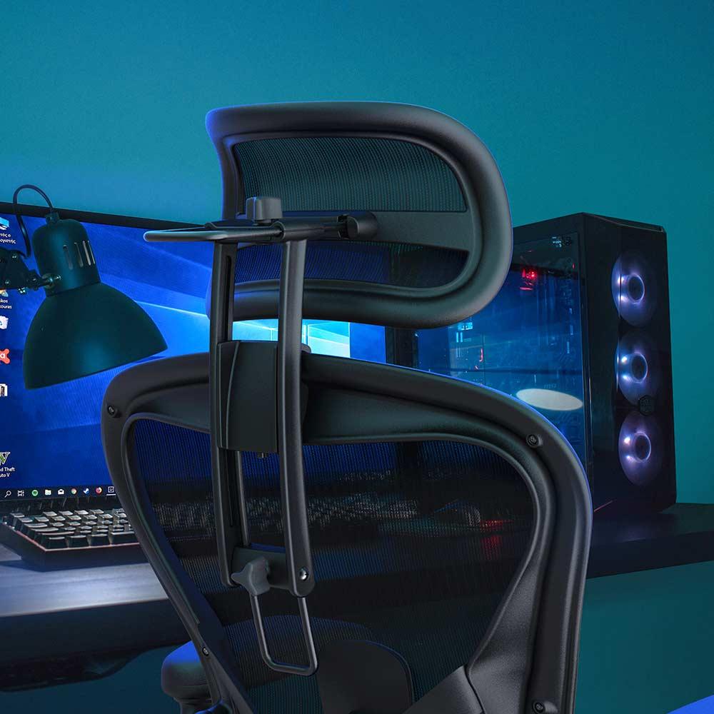 A Refurne Atlas Headrest for Herman Miller Aeron Remastered Chair in graphite is attached to a black ergonomic office chair with mesh back, placed before a computer monitor, glowing gaming PC, and green desk lamp against a teal wall.