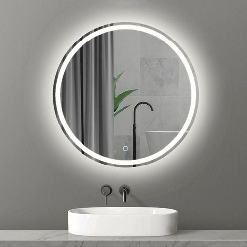A modern bathroom features the Refurne Smart LED Bathroom Mirror – Round, frameless with adjustable lighting and defogging, above a white oval sink and black faucet on a gray wall, reflecting a green plant and bathtub.