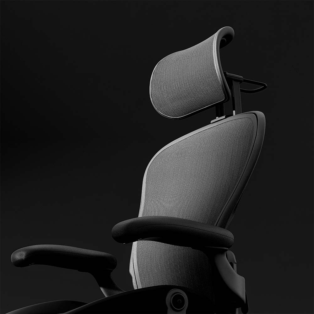 The Refurne Atlas Headrest for Herman Miller Aeron Remastered Chair in Graphite adds contoured ergonomic support, mesh comfort, and adjustable armrests, shown against a dark background.