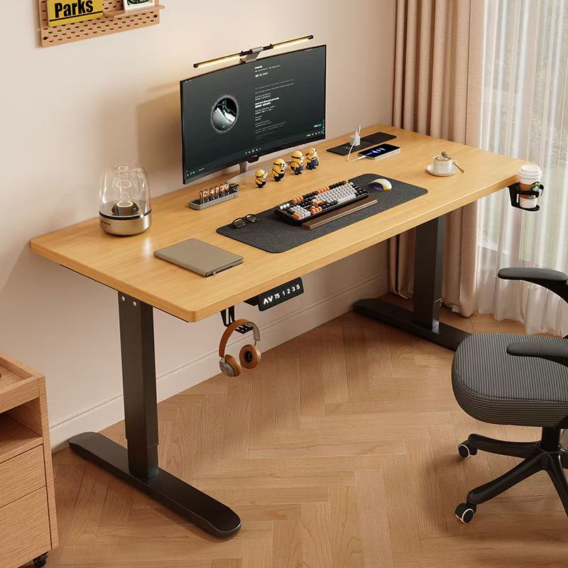 The Refurne Electric Height Adjustable Stand-Up Desk features a beige tabletop, black frame, and control panel. On top are a monitor, keyboard, mouse, lamp, laptop, and figurines. Paired with a chair, headphones, and a coffee cup beside it.