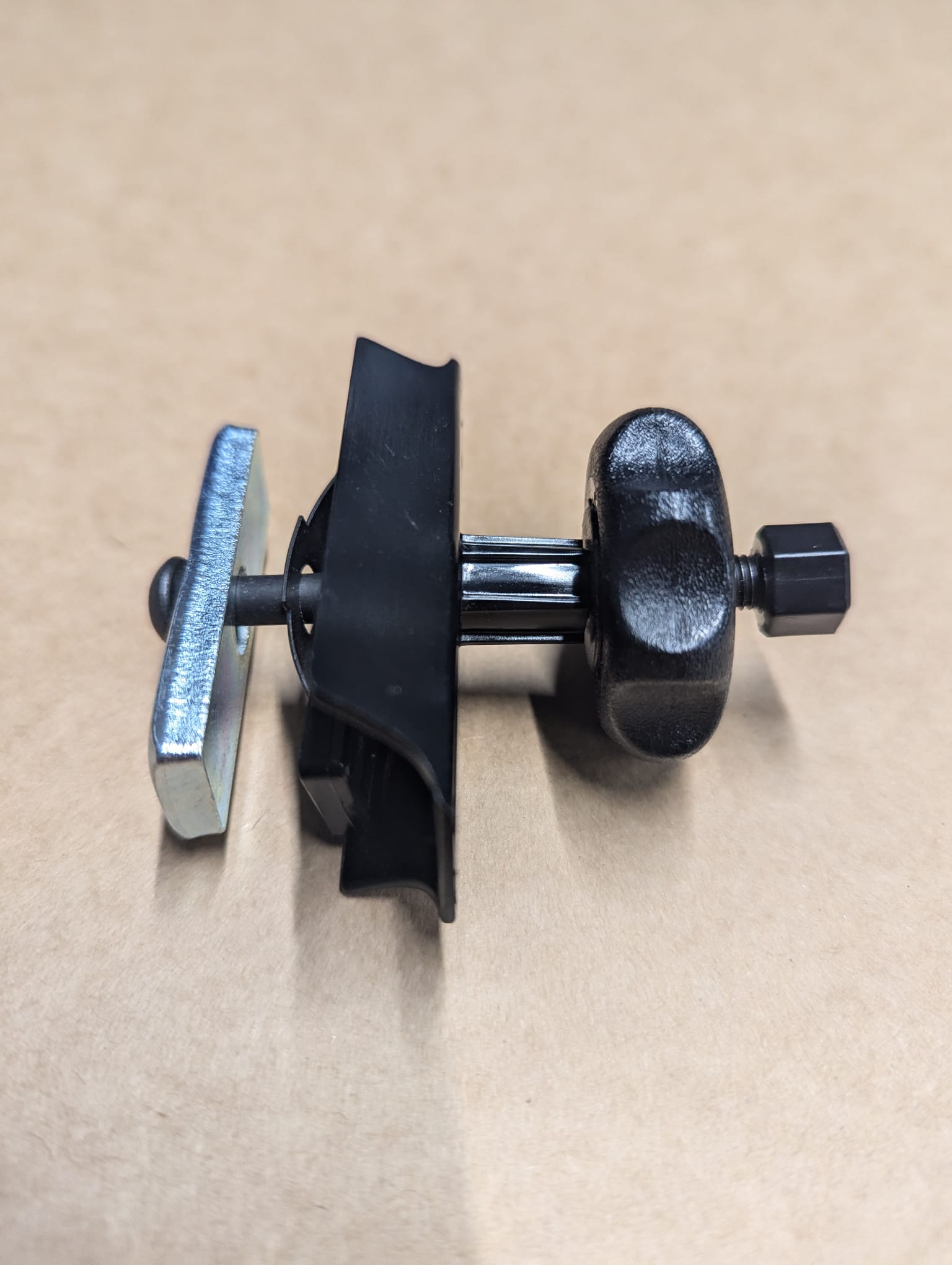 A close-up of a Refurne Roller/Wheel Arm Mechanism for Herman Miller Classic Aeron Chair MK1, featuring metal and black plastic parts with a knob and screw, photographed on a plain light brown surface.