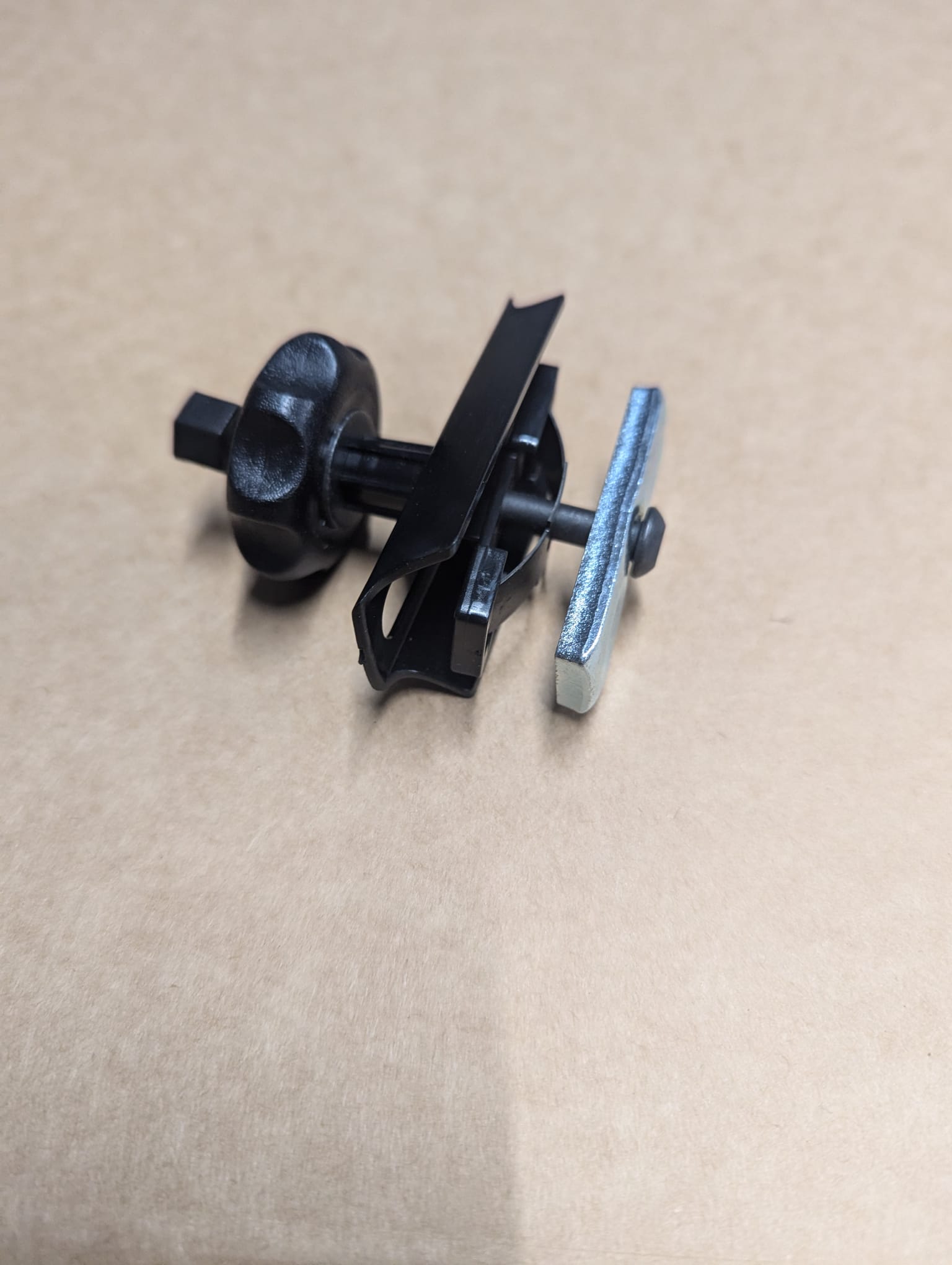 A close-up of the Refurne Roller / Wheel Arm Mechanism for Herman Miller Classic Aeron Chair MK1, featuring a black plastic knob and metal wing, displayed on a plain brown surface.