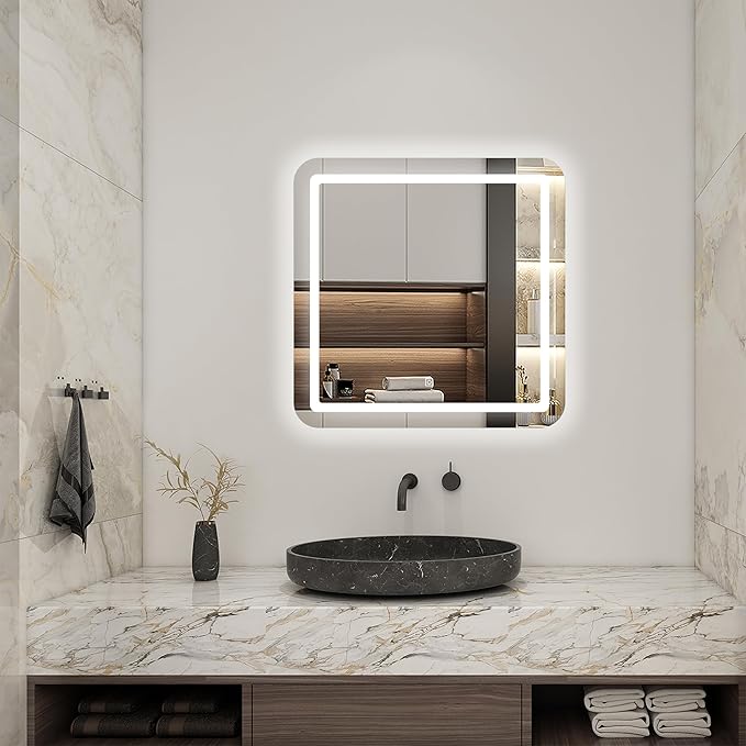 A modern bathroom with marble walls and countertop, a round black stone sink, a black faucet, a gray vase with dried flowers, and the Refurne Smart LED Bathroom Mirror – Square (white light, defogging, frameless) reflecting shelves and cabinets.